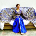 a woman sitting on a couch covered in a blue and gold blanket