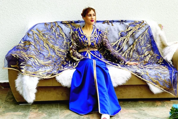a woman sitting on a couch covered in a blue and gold blanket